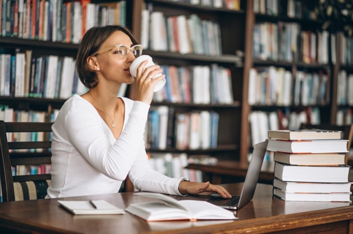 Mulher bebendo café em biblioteca lendo livros