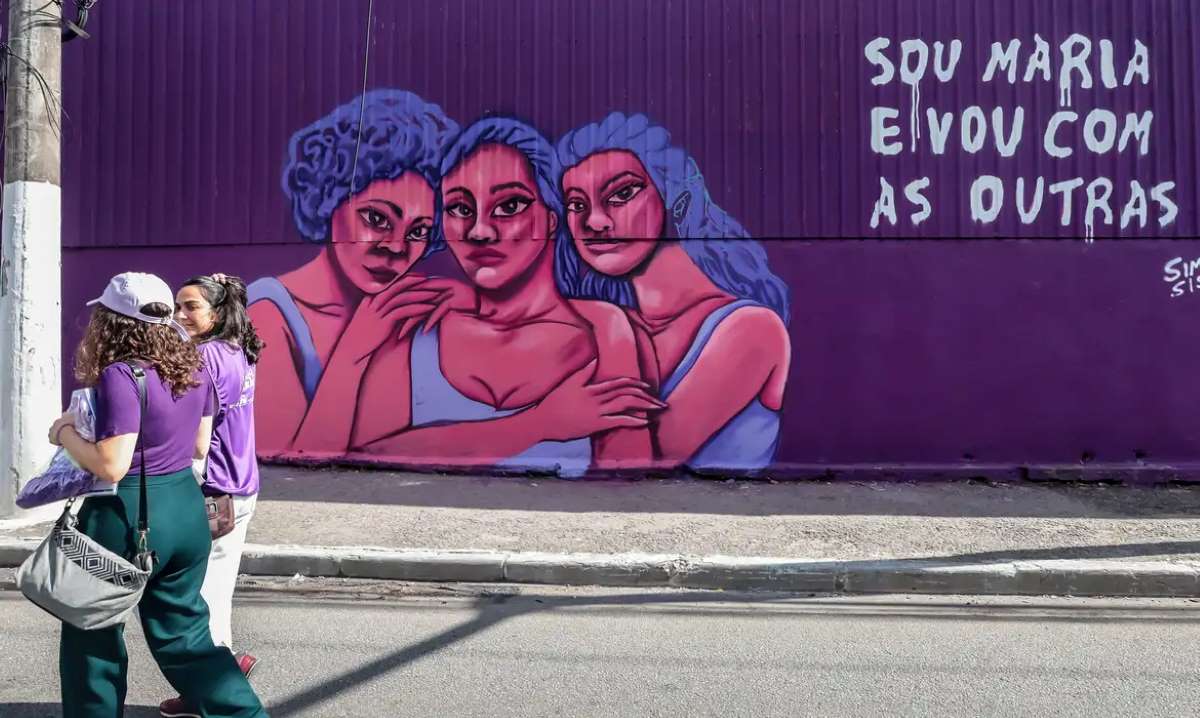 Mulheres andando passando por mural escrito 